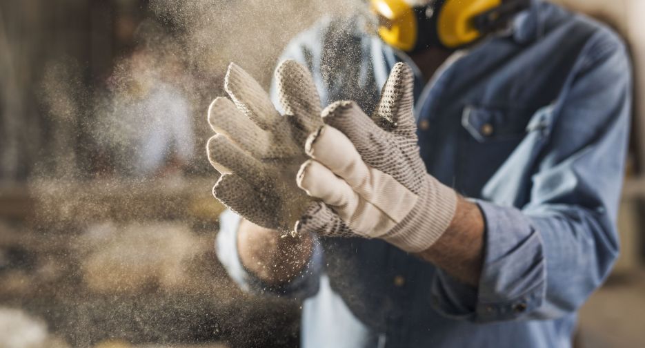 Unrecognizable male hands with work gloves on, clapping to remove sawdust